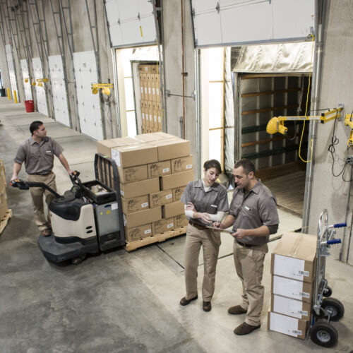 Uniformed warehouse workers loading boxed products into  truck in a distribution warehosue.