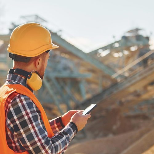 With yellow headphones on neck. Construction worker in uniform is on the quarry.